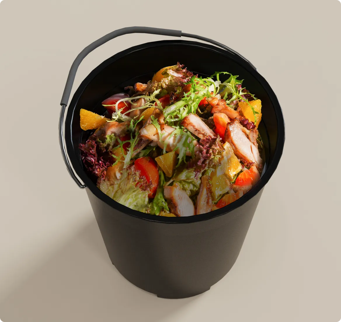 Un seau de cuisine noir rempli de déchets alimentaires variés comprenant de la salade, de la viande et des légumes illustre les déchets ménagers quotidiens typiques.